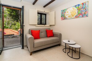 Una habitación con un sofá gris, dos cojines rojos, una mesita redonda y un cuadro abstracto colorido en la pared.
