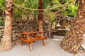 Eine rustikale Outdoor-Szene mit einem Holztisch, einer Steinmauer und einer Lichterkette.