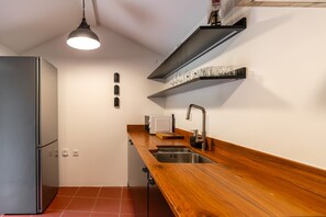 Cocina compacta con refrigerador de acero inoxidable, encimera de madera, pileta integrada y lámpara colgante.