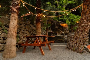 Eine rustikale Outdoor-Szene mit einem Holztisch, Lichterketten und einer Steinmauer.