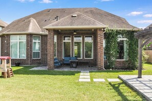 A residential house with a brick exterior, a covered patio with outdoor furniture, and a well-maintained lawn. - Katy Retreat - 5 Bed -Pergola- 5 min to Katy Mills (Katy)