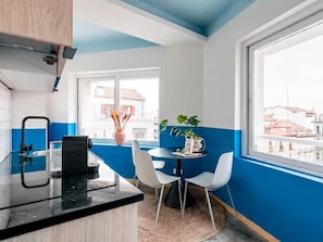 A modern kitchen with a black countertop, white chairs, and a window with a view of buildings.