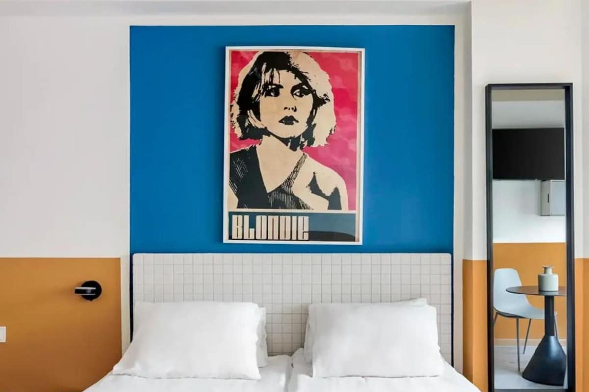 A hotel room with a bed, a wall-mounted artwork, a mirror, and a small table with a chair.