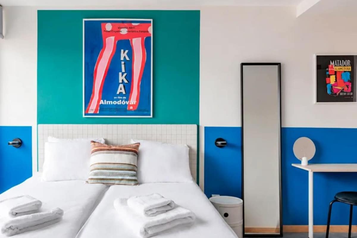 A hotel room with a bed, pillows, towels, a mirror, and a poster on the wall.