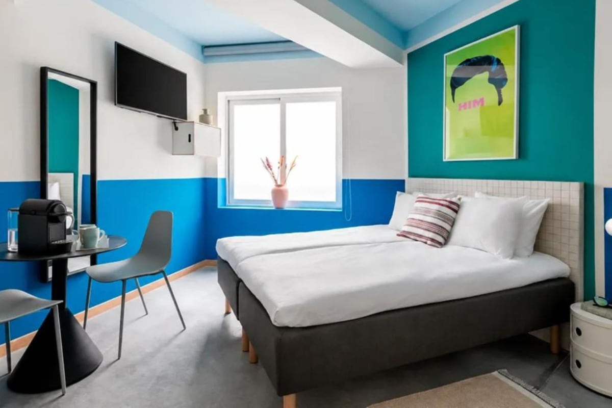 A modern hotel room with a bed, a desk, a chair, a TV, and a window with a view.