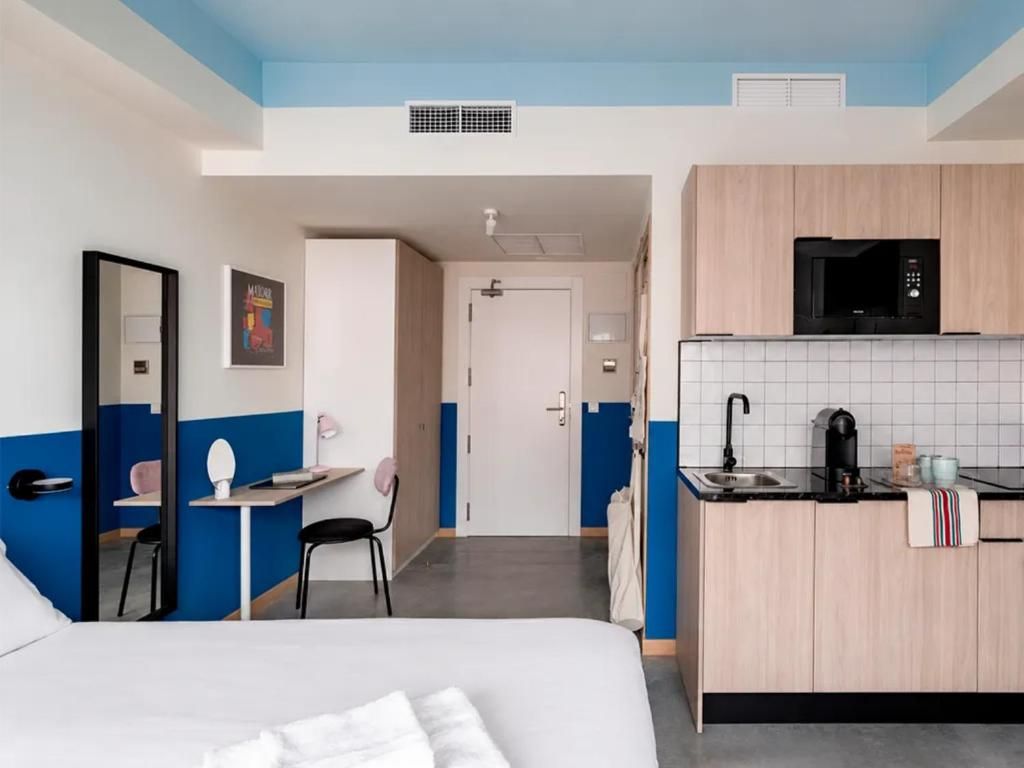 Une chambre d’hôtel comprenant un lit, un bureau, une chaise, une kitchenette équipée d’un four à micro-ondes et une salle de bain.