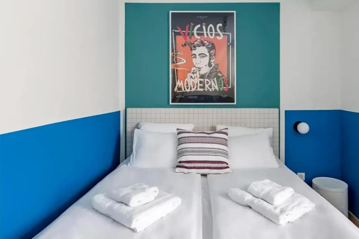 A hotel room with a bed, pillows, and a poster on the wall.