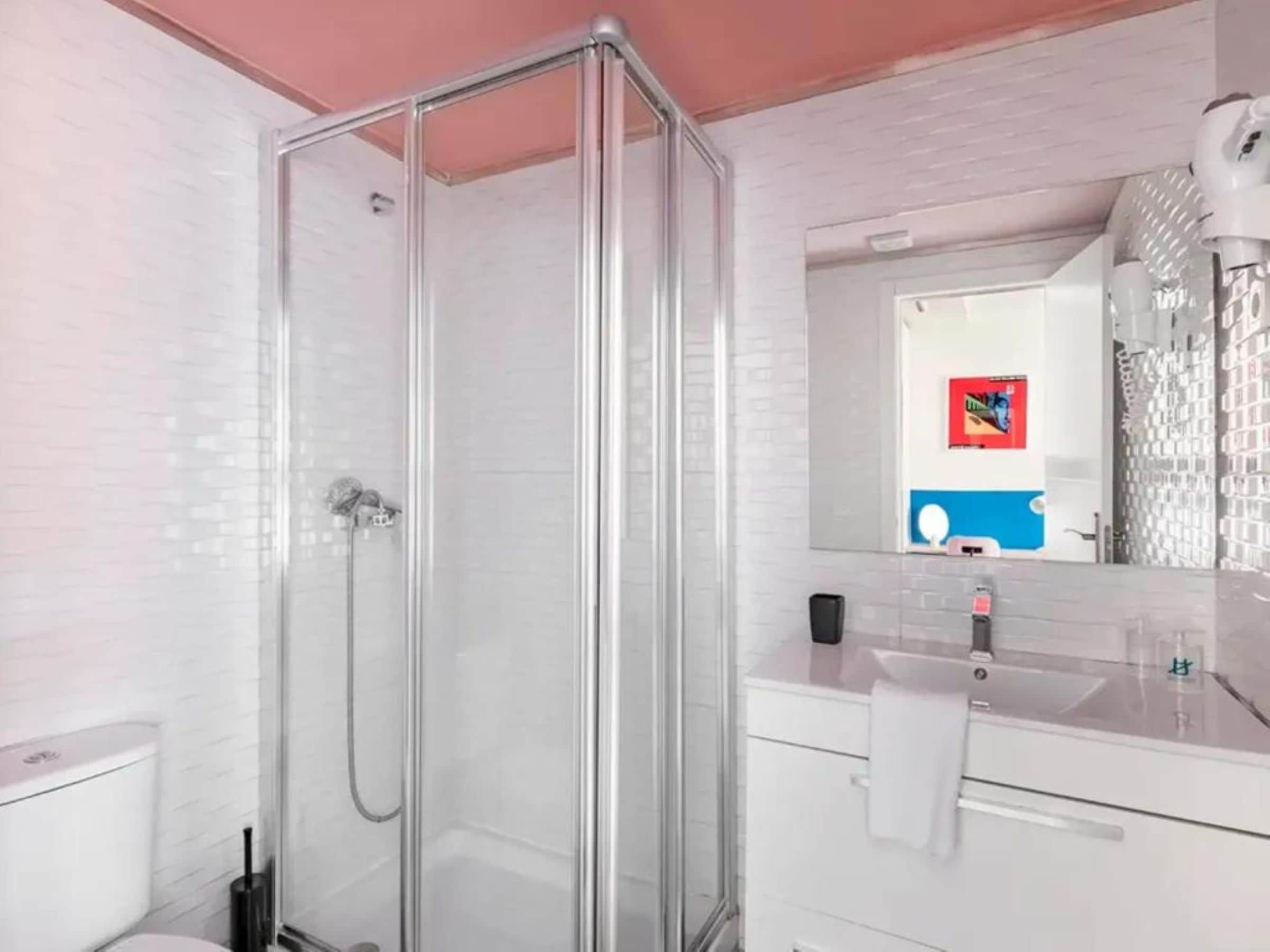 Une salle de bain moderne avec une douche à parois de verre, des murs recouverts de carreaux blancs et un meuble-lavabo blanc avec un miroir.