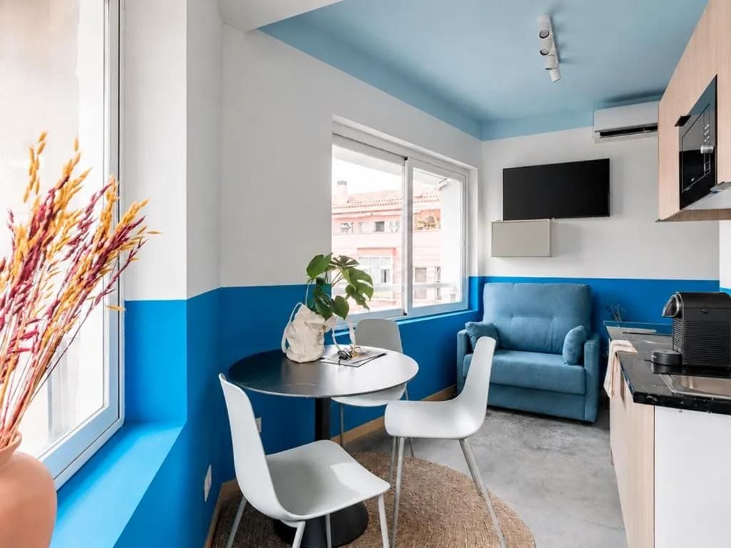 Une cuisine moderne avec un mur d’accent bleu, un coin repas avec une table ronde et des chaises blanches, et un canapé bleu.
