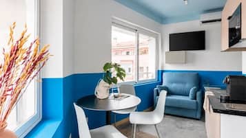 Une cuisine moderne avec un mur d’accent bleu, un coin repas avec une table ronde et des chaises blanches, et un canapé bleu.