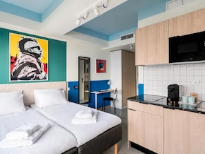 A hotel room with a bed, a desk, a kitchenette, and a bathroom.