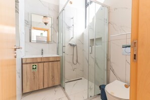 Ein Badezimmer mit Duschkabine aus Glas, einem hölzernen Waschtisch und einer Toilette.