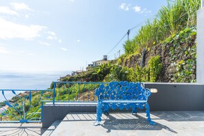 A blue bench on a terrace overlooking a coastal area with a view of the sea and a hillside with vegetation. - Casa Hui Nosso Jardim by Atlantic Holiday (Calheta)