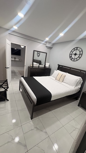 Ein modernes Schlafzimmer mit Bett, Nachttischen, einem Spiegel und einer Wanduhr.