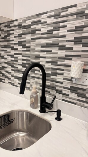 Ein Küchenspülbecken mit einem modernen Wasserhahn, einem Seifenspender und einer Fehlerstromschutzleitung an der Wand.