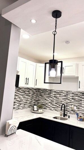 Una cocina moderna con armarios blancos, una lámpara colgante negra y salpicadero de azulejos.