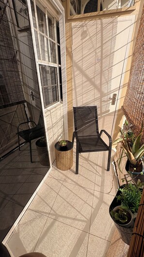 A sunlit balcony with a black chair, a small table with a plant, and potted plants. - Modern 1 Bedroom Apartment Centrally Located in the heart of Kingston (Kingston)