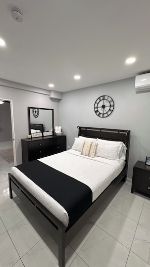 A modern bedroom with a bed, bedside tables, a mirror, a clock, and an air conditioning unit. - Modern 1 Bedroom Apartment Centrally Located in the heart of Kingston (Kingston)