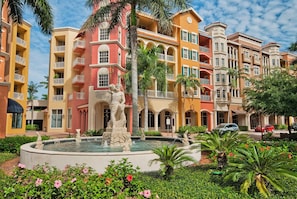 A multi-story hotel with a central courtyard featuring a fountain and statues, surrounded by lush greenery and palm trees. - Bayfront Naples – Downtown Waterfront Living with Rooftop Pool & Restaurants (Naples)