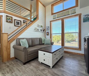 A living room with a staircase, a sofa, a coffee table, and a window with blinds.
