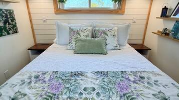 A bedroom with a large bed, a window with plants, and a wall-mounted shelf.