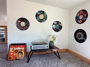 A room with a carpeted floor, a vintage record player on a small table, and a vinyl record wall decoration.