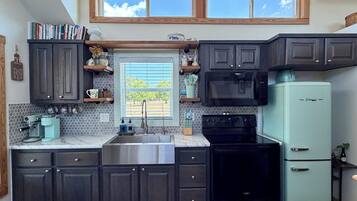 A kitchen with dark cabinets, a stainless steel sink, a black stove, a light blue refrigerator, and a window with blinds.