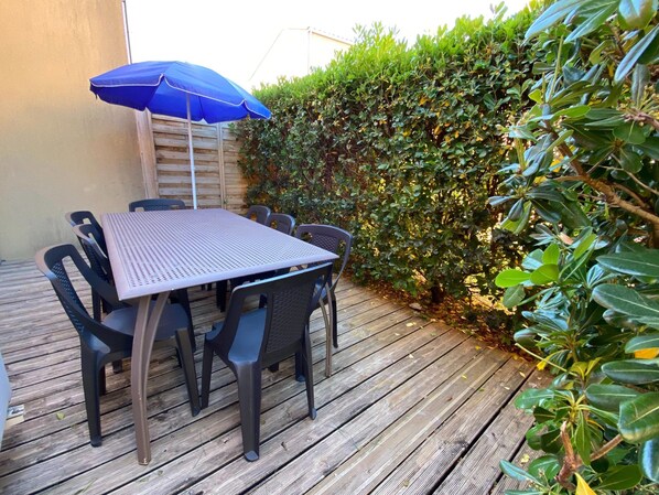 An outdoor patio with a table and chairs, a blue umbrella, and a wooden deck. - Provencal Family Getaway for Six (L'Isle-sur-la-Sorgue)