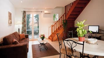 Una sala de estar con un sofá marrón, una mesa de comedor con sillas, una escalera y una planta en maceta.