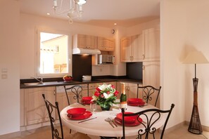 A modern kitchen with wooden cabinets, a dining table set for four, and a chandelier. - Provencal Family Getaway for Six (L'Isle-sur-la-Sorgue)