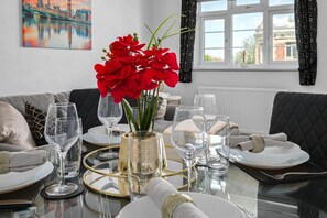 Ein Esstisch ist gedeckt mit klarem Glas, einer Vase mit roten Blumen und einem Gemälde einer Brücke an der Wand.