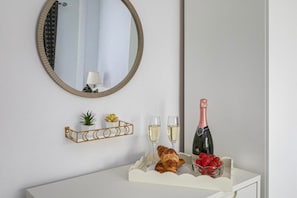 Ein weißer Waschtisch mit Spiegel, ein goldrahmiges Regal mit Pflanzen, zwei Gläser Weißwein, eine Champagnerflasche und ein Croissant.