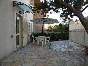 An outdoor patio with stone flooring, a table and chairs, and a large umbrella. - VACATION HOME IN SOUTHERN SARDINIA (Carbonia)