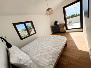 Ein Schlafzimmer mit einem Bett, einem kleinen Fenster, einer Kommode und Blick ins Freie.