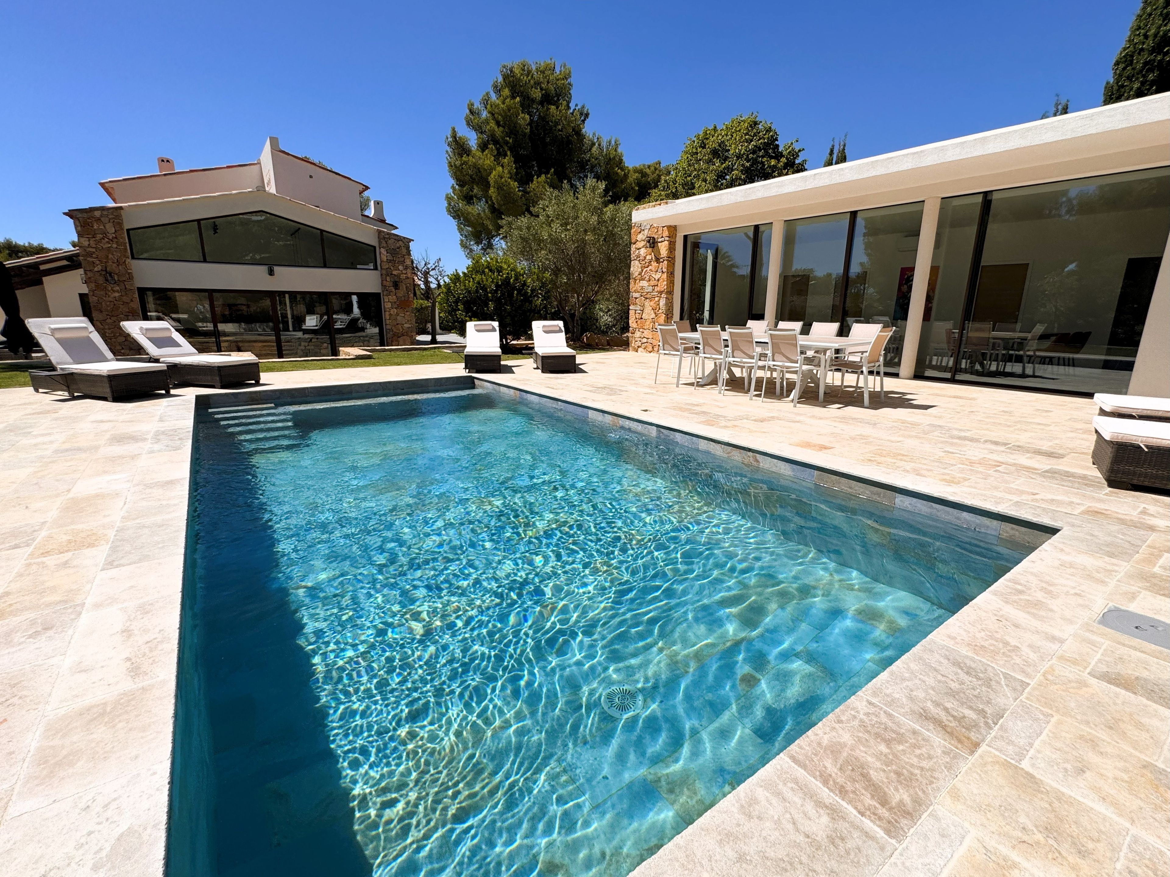 A rectangular swimming pool with clear water, surrounded by lounge chairs and a patio area with outdoor furniture.