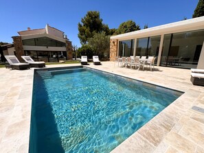 Ein rechteckiger Swimmingpool mit klarem Wasser, umgeben von Liegestühlen und einer Terrasse mit Gartenmöbeln.