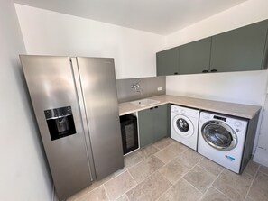 Eine kompakte Küche mit Edelstahl-Kühlschrank, integriertem Geschirrspüler und einer Waschmaschine mit Frontlader.