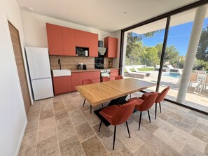 A modern kitchen with red cabinets, a wooden dining table, and a view of a swimming pool. - Villa Mimosa with Private Pool (Saint-Cyr-sur-Mer)