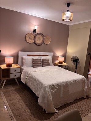 Ein Schlafzimmer mit einem großen Bett, zwei Nachttischen, einer Wandlampe, einem Deckenventilator und Wanddekoration.