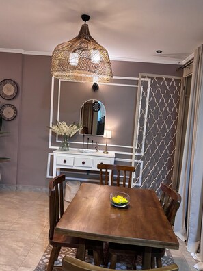 Een eetruimte met een houten tafel, stoelen, een decoratieve hanglamp, een spiegel en een wand met een patroon.