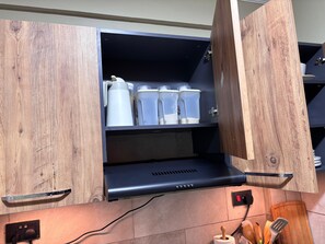 A kitchen with wooden cabinetry, a black range hood, and various kitchen utensils. - Cozy 2BR Apartment with Tarmac Access (Kampala)