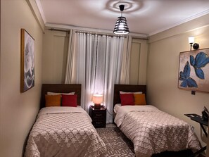 Een hotelkamer met twee bedden, een plafondventilator, een schilderij en een nachtkastje met een lamp.