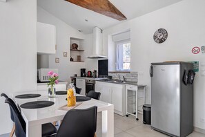 A modern kitchen with white cabinetry, a stainless steel refrigerator, and a dining area with a white table and chairs.