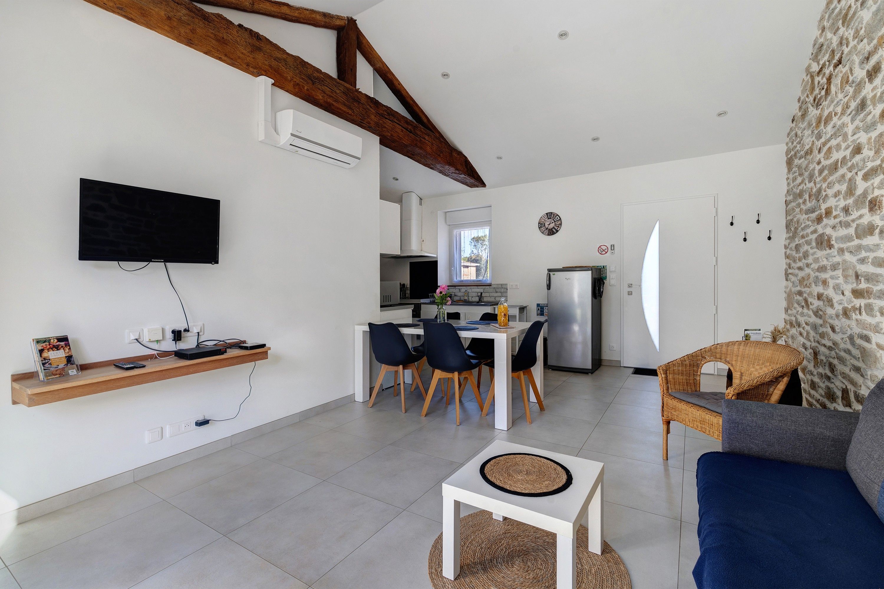 A modern kitchen with a dining area, a flat-screen TV mounted on the wall, and a stone wall.