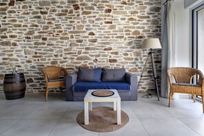 A room with a stone wall, a sofa, two wicker chairs, a small table, and a floor lamp.