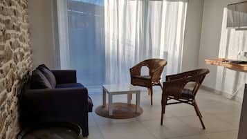 Un saló amb un sofà, dues cadires de vimetla, una taula de centre, un gran canó i una televisió sobre una prestatgeria de fusta.