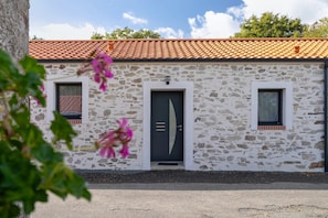 A stone building with a tiled roof, two windows, and a door.