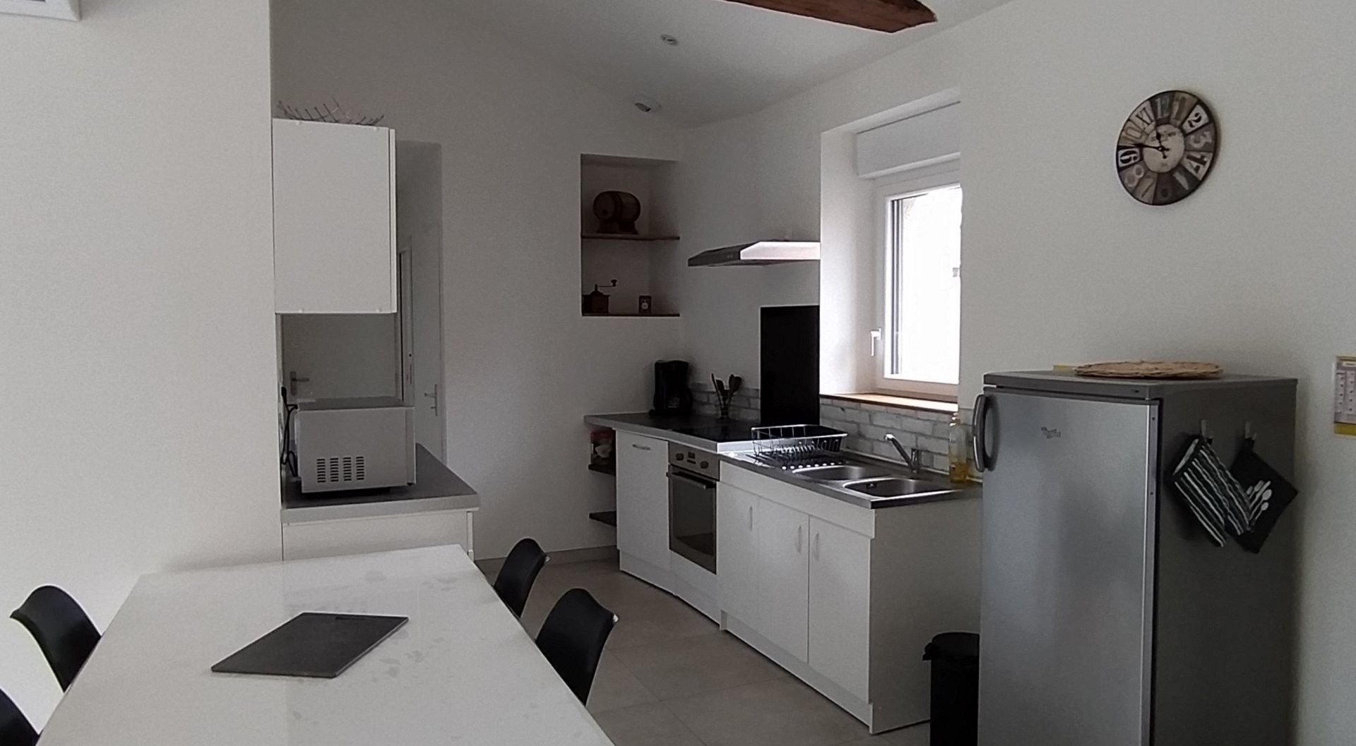 A compact kitchen with a dining table, a refrigerator, a stove, and a window.