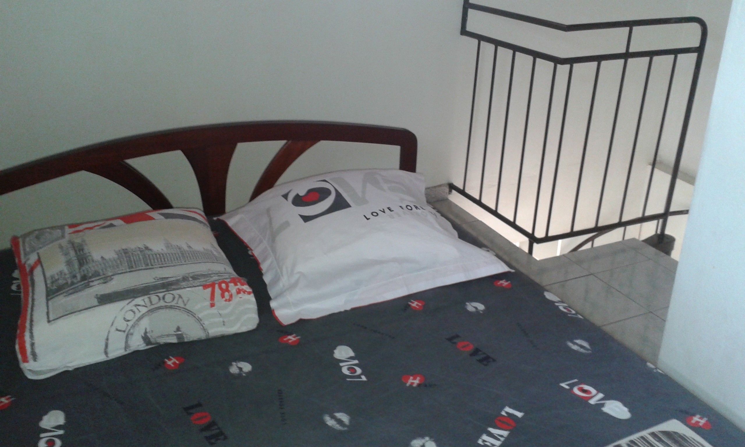 Ein Bett mit einer dunkel gemusterten Tagesdecke und Kissen, eines mit Motiv eines Londoner Wahrzeichens.