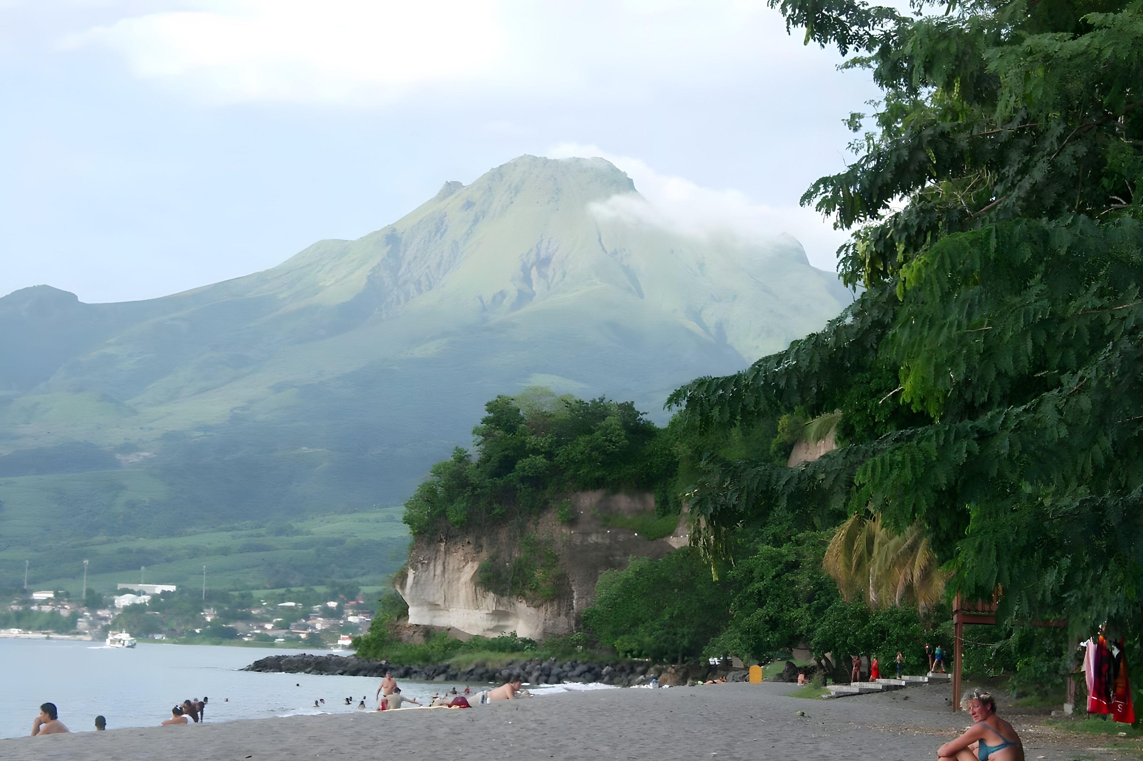 Une plage avec une montagne en arrière-plan, un ciel dégagé et quelques personnes.